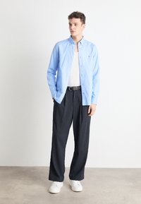 Camicia azzurra chiara con bottoni, canotta bianca, pantaloni a strisce nere e sneakers bianche. Design semplice con tessuto morbido e vestibilità casual.