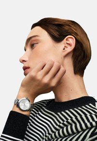 Profiilipilt inimesest, kellel on lühikesed pruunid juuksed, seljas must-valge triibuline suhtel ja vasakul randmel hõbedane käekell.