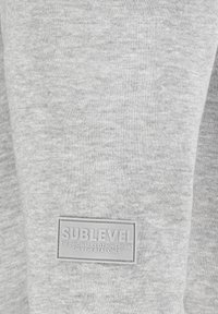Graues Sweatshirtgewebe mit weicher Textur; verfügt über ein rechteckiges graues Etikett mit geprägt "SUBLEVEL" und zusätzlichem Text.
