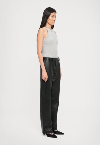 Woman with long straight hair wearing a gray sleeveless top, black leather wide-leg pants, and black pointed flats, standing sideways.