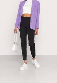 Blazer violet clair, crop top blanc à côtes, pantalons noirs ajustés et baskets blanches à plateforme ; accessoirisé d'un petit sac à main blanc.