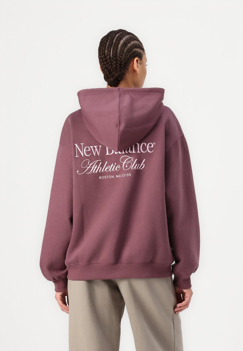 Sudadera con capucha en color malva, que presenta una capucha y un gran texto gráfico blanco en la parte trasera. Puños y dobladillo de canalé con un diseño de corte relajado.