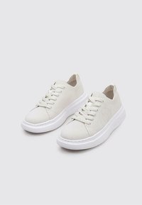 Zapatillas de punto blancas con un upper texturizado, puntera redonda y suela de goma blanca. Presenta cordones y un sutil detalle del logotipo en el lateral.