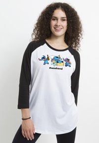 Hvid raglan t-shirt med sorte ærmer, der har farverige tegneseriefigurer og teksten "#weekend" trykt på forsiden. Blødt, afslappet stof.