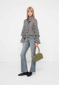 Melnbaltā pārbaudītā blūze ar viļņotām piedurknēm, apvienota ar gaiši ziliem džinsiem ar platām kājām un melnajiem plakanajiem apaviem. Tur rokās zaļu somu.