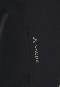 Tela negra con una textura suave que presenta el logo "VAUDE" en gris claro. El material parece duradero con costuras limpias.