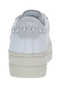 Sneaker bianca con tomaia in pelle liscia, tallone in suede grigio, borchie metalliche e un design minimalista. Presenta una suola testurizzata.