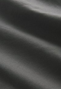 Gros plan sur un tissu gris foncé lisse avec une texture subtile en diagonale et des plis doux créant des ombres et des reflets délicats.