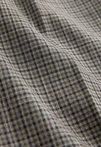 Tissu en laine gris et noir avec un petit motif à carreaux, présenté en gros plan avec une texture et des plis visibles.