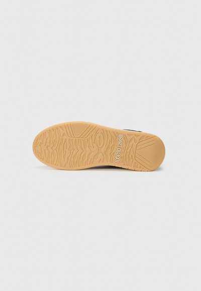 Sola de borracha castanha clara de um sapato com piso texturizado e o logótipo "roberto cavalli" próximo ao calcanhar sobre um fundo branco simples.