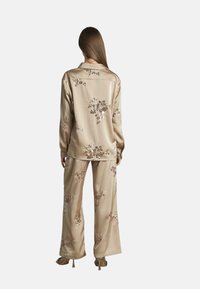 Ensemble de vêtements de détente en satin beige avec broderie florale, chemise boutonée à manches longues et pantalon à jambes larges. Texture lisse, design fluide.