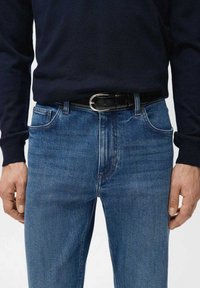 Vaqueros de mezclilla azul con un corte ajustado, que cuentan con bolsillos delanteros y sutiles desgastes, combinados con un cinturón de cuero negro y un suéter oscuro.