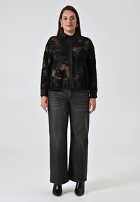 Black sheer blouse with floral embroidery, buttoned front, and collar. Paired with wide-leg dark gray jeans and black heeled boots.
