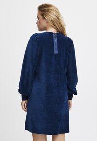 Dunkelblauses Corduroykleid mit langen Puffärmeln und einem Reißverschluss auf der Rückseite. Das Kleid zeichnet sich durch eine weiche Textur und einen lockeren, knielangen Schnitt aus.