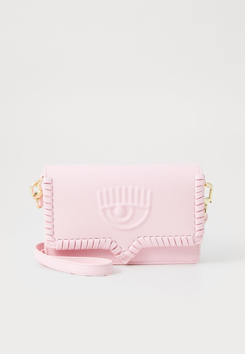 Bolso cruzado de cuero sintético rosa con diseño de ojo en relieve y borde decorativo trenzado. Correa ajustable y herrajes en color dorado.
