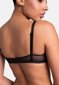 Soutien-gorge en dentelle noire avec bretelles ajustables, présentant un design en maille, des bords festonnés et une fermeture à crochets au dos. Matériau texturé.