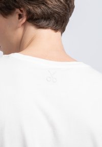 Witte katoenen T-shirt met een ronde hals, voorzien van een subtiel geborduurd scharenlogo op de bovenrug nabij de hals. Soepele textuur.