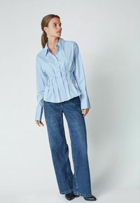 Light blue fitted shirt with a cinched waist, long sleeves, and button front; paired with wide-leg dark denim jeans.