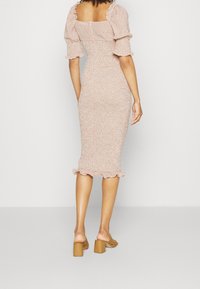 Robe midi fleurie rose clair avec manches bouffantes, silhouette ajustée et ourlet à volants. Portée avec des sandales à talons blocs marron.