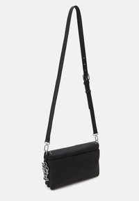 Sort rektangulær crossbody-taske med justerbar rem og spænde i sølv, med en lille nøglering af en tegneseriefigur på siden.