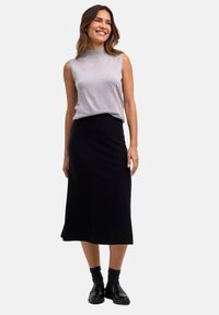 Top grigio senza maniche e gonna nera lunga fino al ginocchio realizzata in tessuto elastico. Scarpe nere e calze scure completano l'outfit. Design semplice e minimalista.