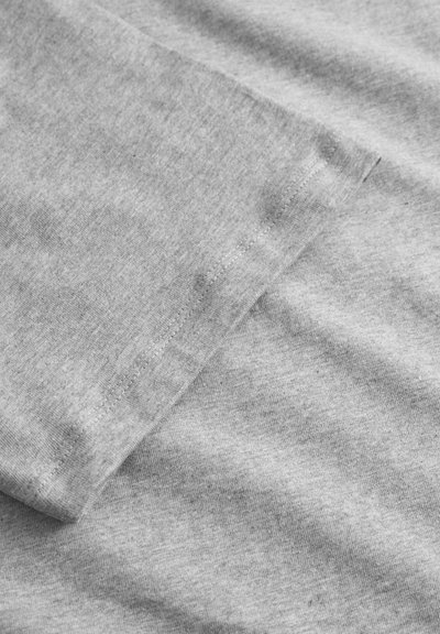 Tissu en coton gris avec une texture lisse, présentant un motif légèrement chiné et des coutures visibles le long des bords.