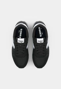 Black athletic sneakers with white and gray accents, featuring a textured upper, round toe, and lace-up design. Label on tongue visible.