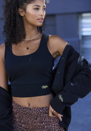 Schwarzes geripptes Crop-Top mit gelbem Logo, kombiniert mit einer schwarzen übergroßen Jacke, die über leggings mit Leopardenmuster getragen wird. Glatte Textur insgesamt.