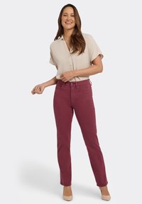 Bourgondische jeans met hoge taille gecombineerd met een lichtbeige blouse met korte mouwen en nude pumps; gladde textuur, klassiek ontwerp en op maat gemaakte pasvorm.
