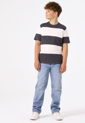 Camiseta de rayas en gris oscuro y blanco roto de algodón, con mangas cortas. Combinada con jeans de mezclilla azul claro y zapatillas blancas.
