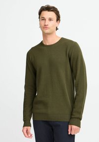 Olive zöld kötött pulóver, texturált, kiemelkedő mintával, bordás mandzsetta és szegély. Feszes fazon, kerek nyakkivágással és hosszú ujjal.