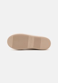 Rubberen zool in lichtbeige met horizontale ribbels voor grip. Heeft een ingebosseld logo in het midden. Over het algemeen een gladde textuur.