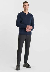 Suéter de polo de punto azul marino con cuello, combinado con pantalones ajustados gris oscuro y zapatos de cuero negros, sobre un fondo liso.