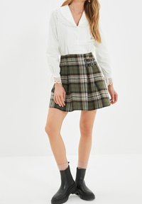 Valkoinen paita, jossa on pitsikaulus, yhdistetty vihreään ruutuhameeseen, jossa on soljet. Mustat nilkkabotit täydentävät asua.