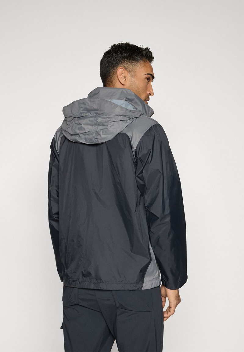 Chaqueta resistente al agua en negro con capucha gris y acentos en los hombros. Presenta una textura suave y un ajuste relajado con capucha ajustable.