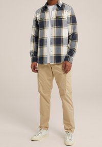 Rutigt flanellskjorta i marinblått, vitt och olivgrönt, med två bröstfickor och knäppning, kombinerad med beigefärgade cargobyxor och vita sneakers.