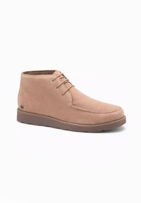 Botines de ante beige con puntera redondeada, diseño de cordones y suela de goma. Presenta costuras mínimas y un detalle del logo en el lateral.
