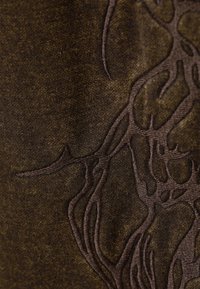 Bruine stof met een subtiel textuurpatroon en donkerbruine verhoogde borduursels die doen denken aan verstrengelde takken. Over het algemeen een soepele textuur.