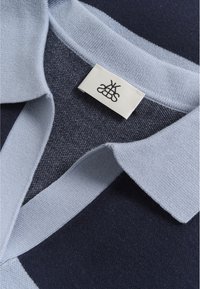 Cămașă polo de culoare bleumarin și albastru deschis, dintr-un material texturat, cu un guler moale. Dispune de o etichetă țesută cu logo negru brodat.