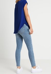 Modrý top s krátkým rukávem a zipem na zadní straně, kombinovaný se světlomodrými skinny džíny a bílými teniskami. Hladký materiál, volný střih.