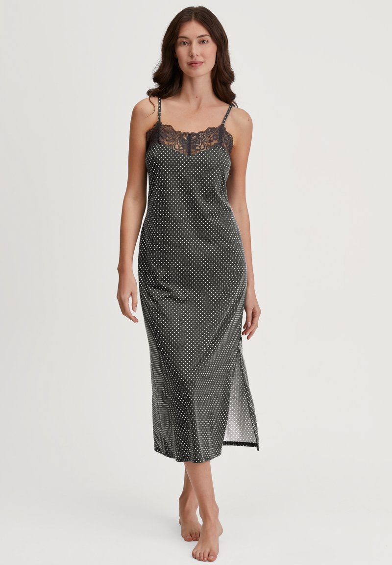 Nightgown nero con pois bianchi, caratterizzato da un delicato profilo in pizzo sullo scollo, spalline sottili regolabili e una fessura laterale per una maggiore libertà di movimento.