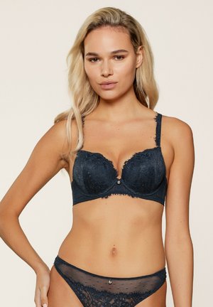 Navy lace bra with underwire support, floral pattern, scalloped edges, and a decorative front jewel. Matching sheer thong included.