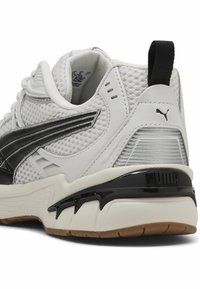 Hvide sneakers med sorte accenter, mesh-overdel, teksturerede sider og en kraftig gummisål. Har et trækstykke og Puma-logo på hælen.
