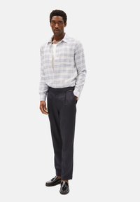 Camicia a quadri blu chiaro e bianca con bottoni, abbinata a pantaloni scuri su misura e mocassini neri. La camicia ha una vestibilità ampia e maniche lunghe.