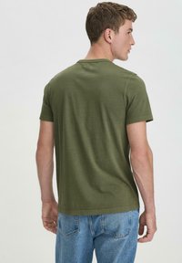 Olivgrünes Baumwoll-T-Shirt mit kurzen Ärmeln, rundem Ausschnitt und klassischem Schnitt, kombiniert mit hellblauen Jeans.