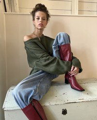 Oversize'owy, oliwkowozielony sweter, jasnoniebieskie spodnie dresowe z czerwonymi akcentami oraz czerwone botki za kostkę z kwadratowym noskiem i obcasem typu block.