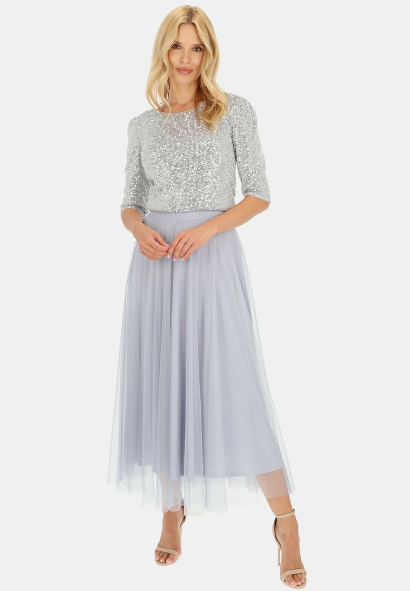 Srebrny top z cekinami i rękawami do trzech czwartych, w połączeniu z jasnoniebieską spódnicą z tiulu o luźnym fasonie i długości do kolan.