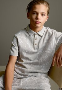 Hellgraues Polohemd mit einem dezenten Blumenmuster, ausgestattet mit einem Kragen und vier Holzknöpfen, kombiniert mit passenden Shorts.