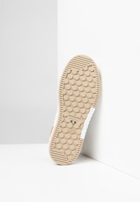 Suola di una sneaker, caratterizzata da una gomma beige con texture circolare, marchiata "NeroGiardini" e contrassegnata con la taglia 37. I bordi sono leggermente rialzati.