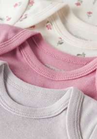 Tre babyheldragter i lyserød, hvid med blomsterprint og lysegrå. Blødt bomuldsmateriale med ribbede halsudskæringer og syningsdetaljer.